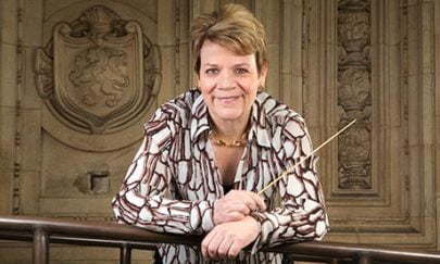 Conductor Marin Alsop leaning on a rail holding a baton